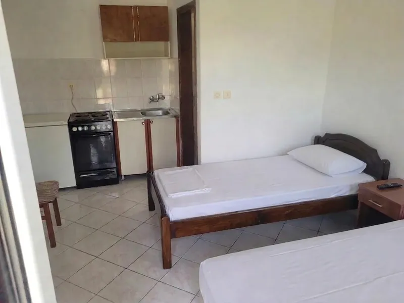 Studio interior with two single beds and a kitchenette along the left wall, with cooker, sink and fridge